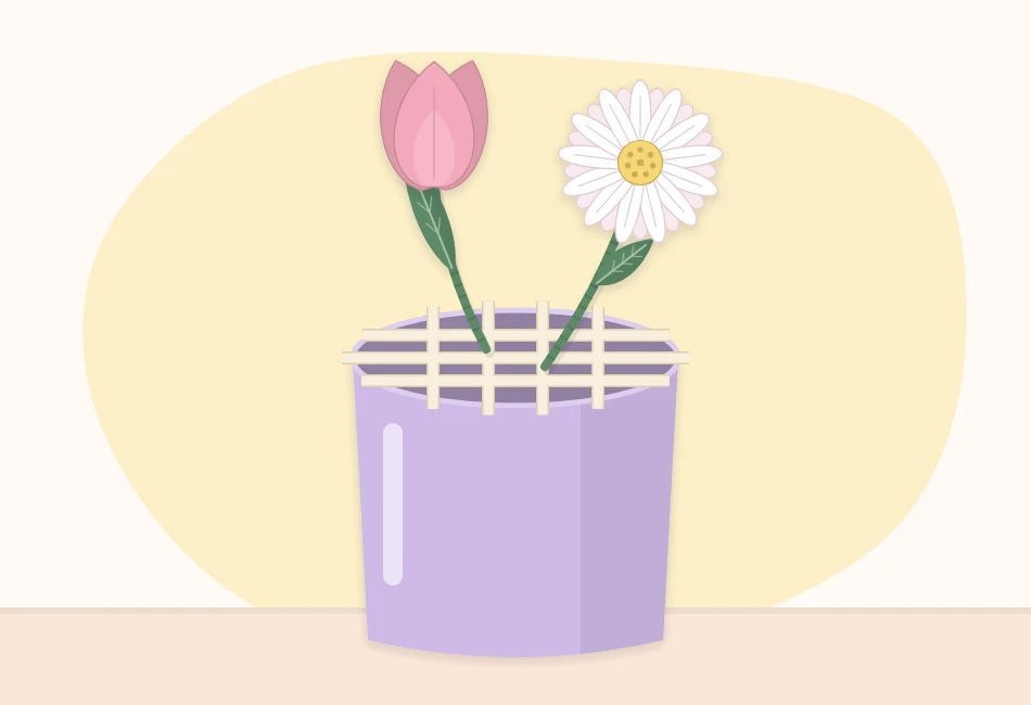 An empty vase with a grid of clear tape across the opening and two tall paper flower stems placed in the center squares