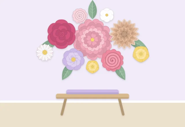 A wall decorated with a cluster of paper flowers in several sizes above a small bench