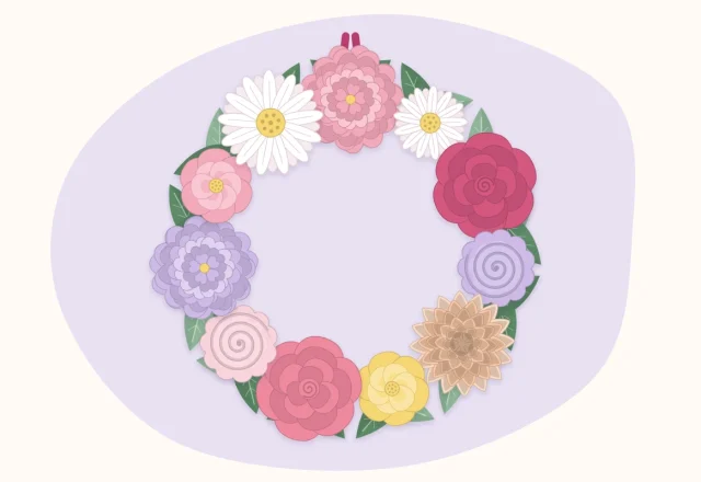 Round wreath covered with paper flowers in pinks and peach with green paper leaves